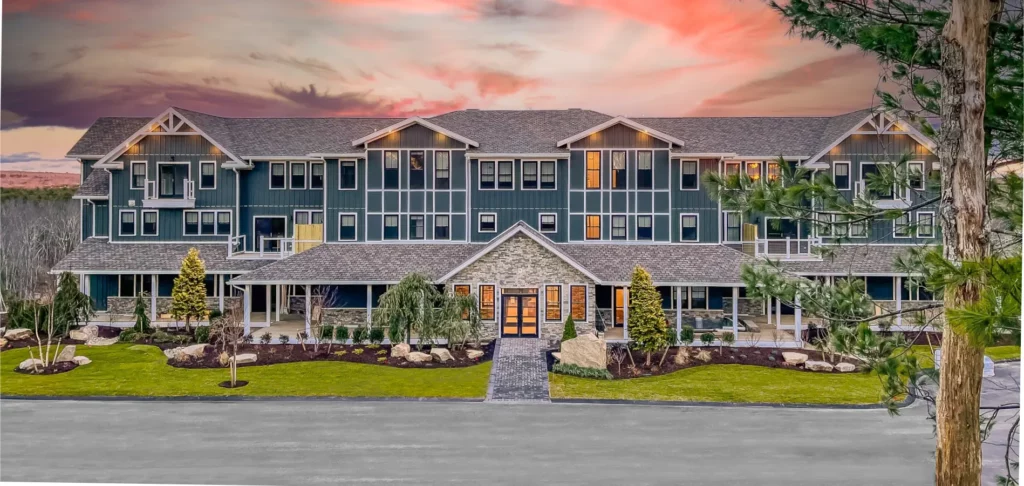 Hilltop Lodge at The Preserve with a stone entrance is surrounded by landscape greenery against a vibrant sunset sky.